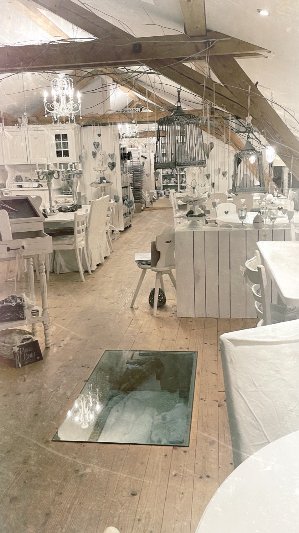Der Laden unter dem Dach: weisse Möbel, Holzboden und in der Mitte ein Glasfenster im Boden